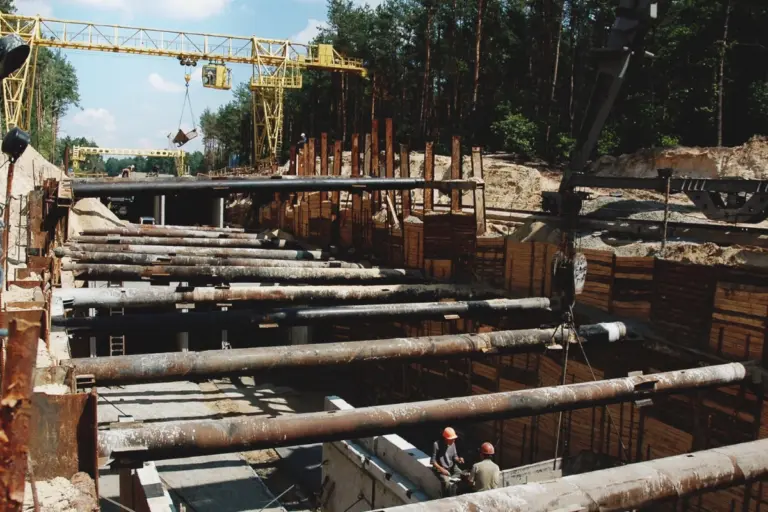 Baustelle im Wald, wo ein Tunnel gegraben wird, umgeben von Bäumen und Baugeräten.